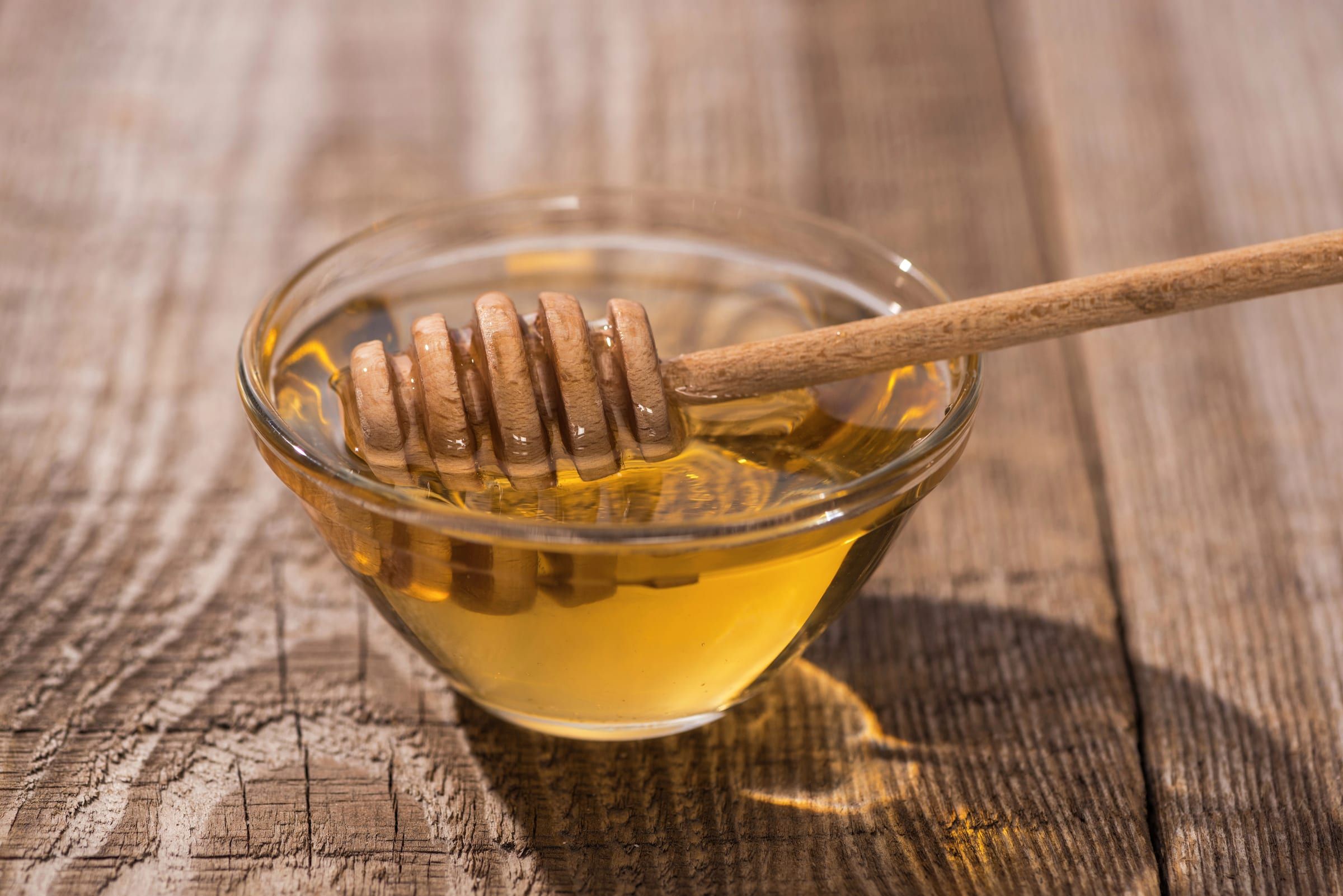 Miel liquide dans un bol en verre avec une cuillère à miel en bois